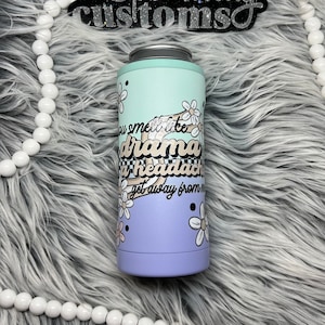 May include: A purple and green insulated tumbler with a white daisy pattern and the text "You smell like drama and a headache, get away from me".