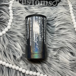 May include: A black and silver tumbler with a white floral design and the word "remarkable" printed on the side. The tumbler is on a white fluffy surface.