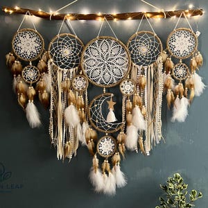 May include: A collection of handmade dream catchers in various sizes, suspended from a wooden branch with fairy lights. The dream catchers feature intricate woven patterns, feathers, and beads in neutral tones.