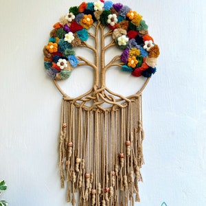 Op de afbeelding: Een macramé wandhanger met een levensboomontwerp met kleurrijke pompoenen en kralen. De boom is gemaakt van natuurlijke jute touw en heeft een ronde vorm. De hanger is versierd met houten kralen en heeft een franje aan de onderkant.