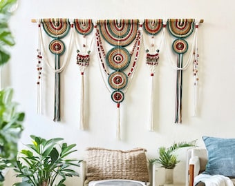May include: A wall hanging made of macrame with a geometric design in shades of green, red, and beige. The hanging features multiple circular shapes and fringe details.