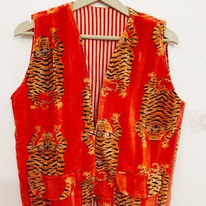 May include: A sleeveless vest in a vibrant orange hue featuring a repeating pattern of black and yellow tigers. The garment has a V-neckline, three front buttons, and two lower pockets. The interior lining displays a vertical red and white stripe pattern.