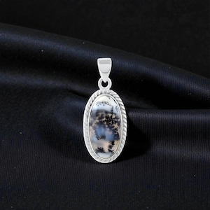 May include: An oval pendant featuring a dendritic agate stone with black fern-like inclusions set in a silver frame with a twisted rope border. The pendant includes a simple silver bail at the top for attachment to a chain or cord necklace.