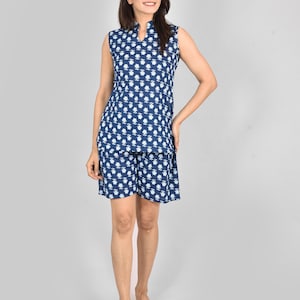 Puede incluir: Un conjunto de pijama azul marino sin mangas con un estampado floral blanco. El conjunto incluye una camiseta con cuello mandar&iacute;n y pantalones cortos a juego. La modelo est&aacute; descalza, de pie frente a un fondo gris claro.