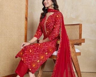 Puede incluir: Un conjunto rojo vibrante de tres piezas que incluye un kurta de manga larga con un patrón tradicional de teñido anudado bandhani en amarillo y blanco, pantalones rojos lisos a juego y un dupatta rojo transparente con borde dorado.