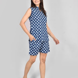 Puede incluir: Un conjunto de pijama azul marino sin mangas con un estampado floral blanco. El conjunto incluye una camiseta con cuello y pantalones cortos a juego. La modelo lleva el conjunto de pijama. La tela parece ligera y c&oacute;moda.