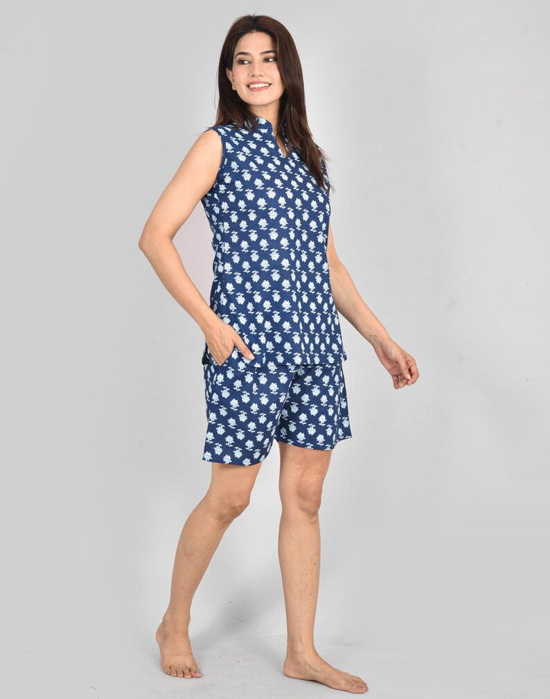Puede incluir: Un conjunto de pijama azul marino sin mangas con un estampado floral blanco. El conjunto incluye una camiseta con cuello y pantalones cortos a juego. La modelo lleva el conjunto de pijama. La tela parece ligera y c&oacute;moda.