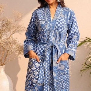 May include: A long-sleeved blue robe featuring a patchwork-style pattern of white circles, swirls, and geometric shapes. The garment includes a tie-waist belt, two front pockets, and a white piped trim along the collar and front opening.