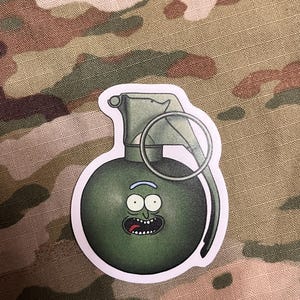 May include: A green cartoon grenade with a face resembling Rick Sanchez from the animated series Rick and Morty. The grenade has a black pull pin and a white background.
