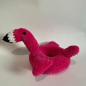 May include: Pink crocheted flamingo shaped ring holder. The flamingo has a white and black beak and a black eye.