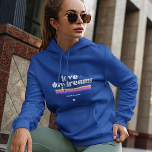 Super soft sweatshirt with front pockets, that say "Love + Daydreams" on the front, a purple and orang rainbow design with the words "dream in color" beneath is.