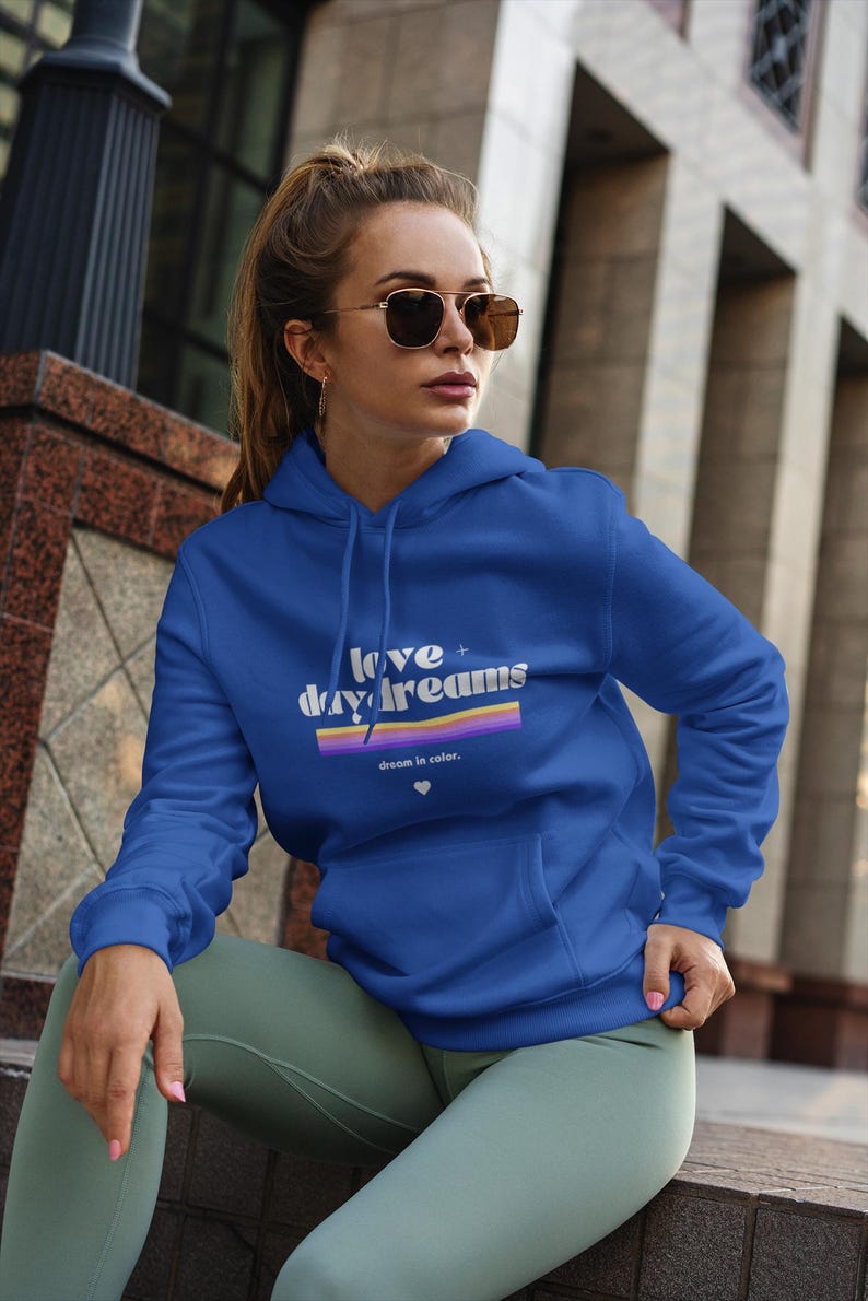 Super soft sweatshirt with front pockets, that say "Love + Daydreams" on the front, a purple and orang rainbow design with the words "dream in color" beneath is.