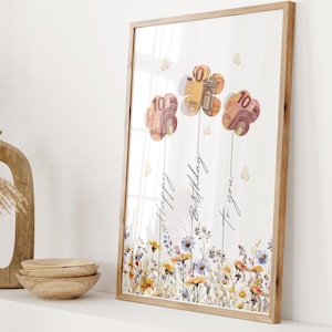 Pode incluir: Uma impressão de arte emoldurada com três desenhos de flores feitos com notas, com o texto "Happy Birthday to you". A obra de arte está sobre um fundo branco com uma borda floral e uma moldura de madeira.