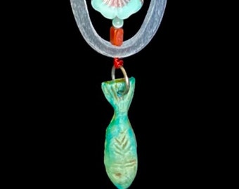 May include: A silver chain necklace with a turquoise and red beaded pendant. The pendant features a turquoise flower with a silver ring around it and a turquoise fish charm hanging below.