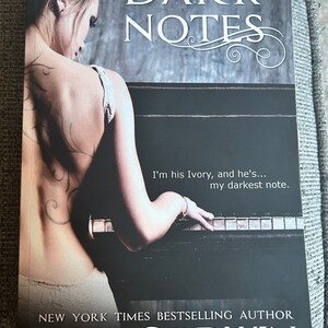 May include: A book cover with the title "DARK NOTES" in large, elegant font. The cover features a woman's back with a tattoo, and a piano. The author's name, PAM GODWIN, is at the bottom. The text "I'm his Ivory, and he's... my darkest note." is also visible.