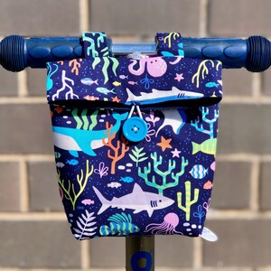 Peut inclure: Un guidon de scooter bleu avec un sac en tissu attach&eacute;. Le sac est d&eacute;cor&eacute; d'une sc&egrave;ne sous-marine color&eacute;e repr&eacute;sentant des requins, des coraux et des poissons. Le sac a une fermeture &agrave; bouton bleu.