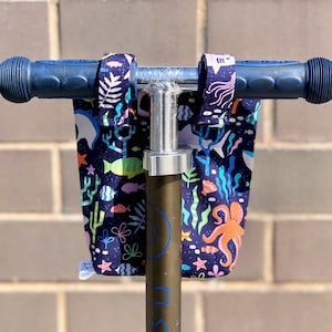 Peut inclure: Un guidon de scooter bleu avec un couvre-guidon en tissu color&eacute; repr&eacute;sentant une sc&egrave;ne sous-marine avec des poissons, des algues et une pieuvre. Le tissu est bleu fonc&eacute; avec des couleurs vives.