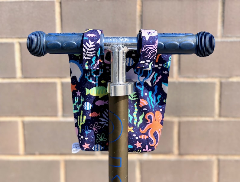 Peut inclure: Un guidon de scooter bleu avec un couvre-guidon en tissu color&eacute; repr&eacute;sentant une sc&egrave;ne sous-marine avec des poissons, des algues et une pieuvre. Le tissu est bleu fonc&eacute; avec des couleurs vives.