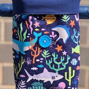 Peut inclure: Un sac de guidon en tissu bleu avec un imprim&eacute; color&eacute; de vie marine. Le sac a une fermeture &agrave; bouton bleu et pr&eacute;sente une vari&eacute;t&eacute; de cr&eacute;atures marines, y compris des poissons, des baleines et des coraux.
