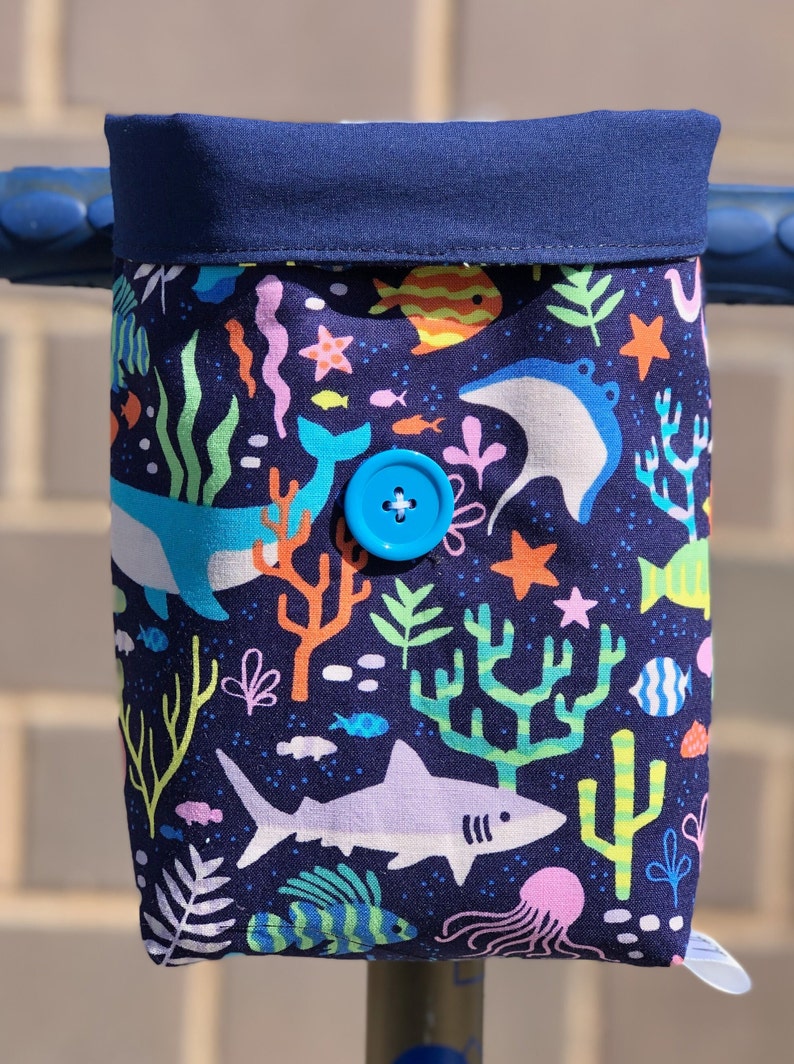 Peut inclure: Un sac de guidon en tissu bleu avec un imprim&eacute; color&eacute; de vie marine. Le sac a une fermeture &agrave; bouton bleu et pr&eacute;sente une vari&eacute;t&eacute; de cr&eacute;atures marines, y compris des poissons, des baleines et des coraux.