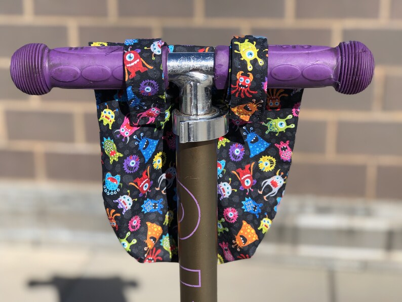 May include: Purple scooter handlebars with black fabric handlebar covers featuring a colorful monster print.