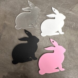 Könnte beinhalten: Vier Hasensilhouetten aus verschiedenen Farben Acryl geschnitten. Die Hasen sind in verschiedenen Schattierungen von Grau, Weiß, Schwarz und Rosa.