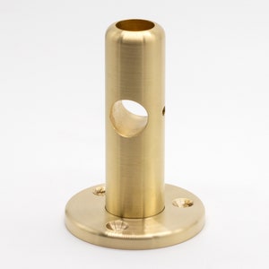 May include: A brass pipe fitting with a round base and a hole in the center. The fitting is polished and has a shiny finish.