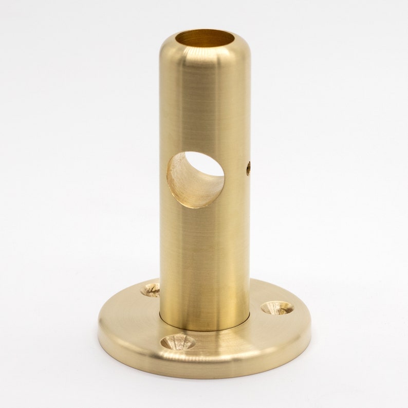 May include: A brass pipe fitting with a round base and a hole in the center. The fitting is polished and has a shiny finish.