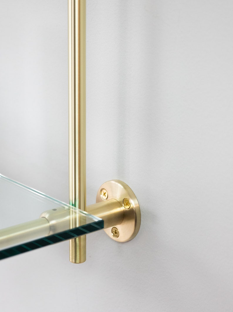 May include: A gold metal shelf bracket with a round base and three screws. The bracket is attached to a glass shelf.