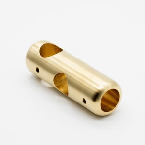 May include: A gold-colored metal tube with two holes and a rounded end. The tube has a smooth, polished finish.