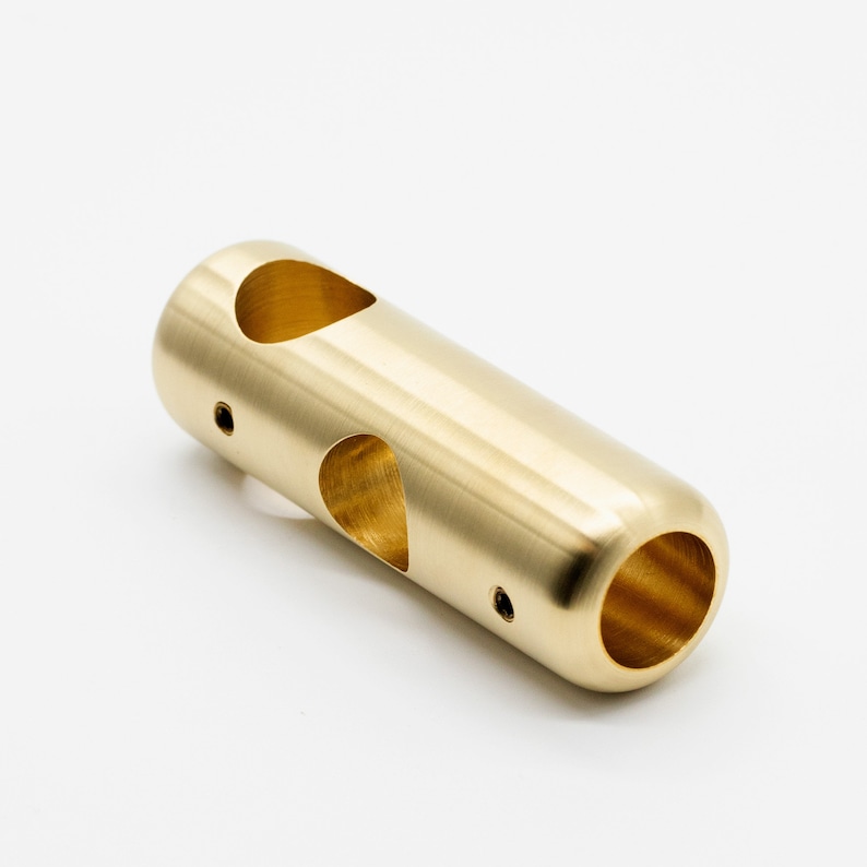 May include: A gold-colored metal tube with two holes and a rounded end. The tube has a smooth, polished finish.