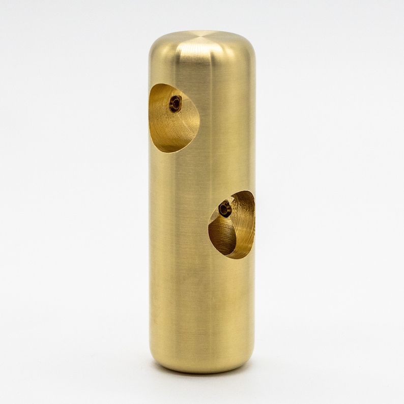 May include: A gold-colored metal cylinder with two circular cutouts. The cylinder has a smooth, polished finish.