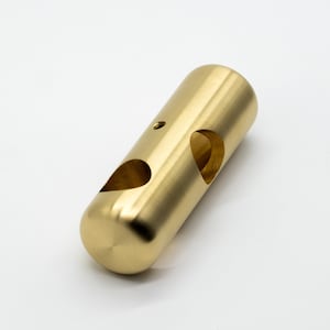 May include: A gold-colored metal cylinder with two heart-shaped cutouts. The cylinder has a smooth, polished finish.