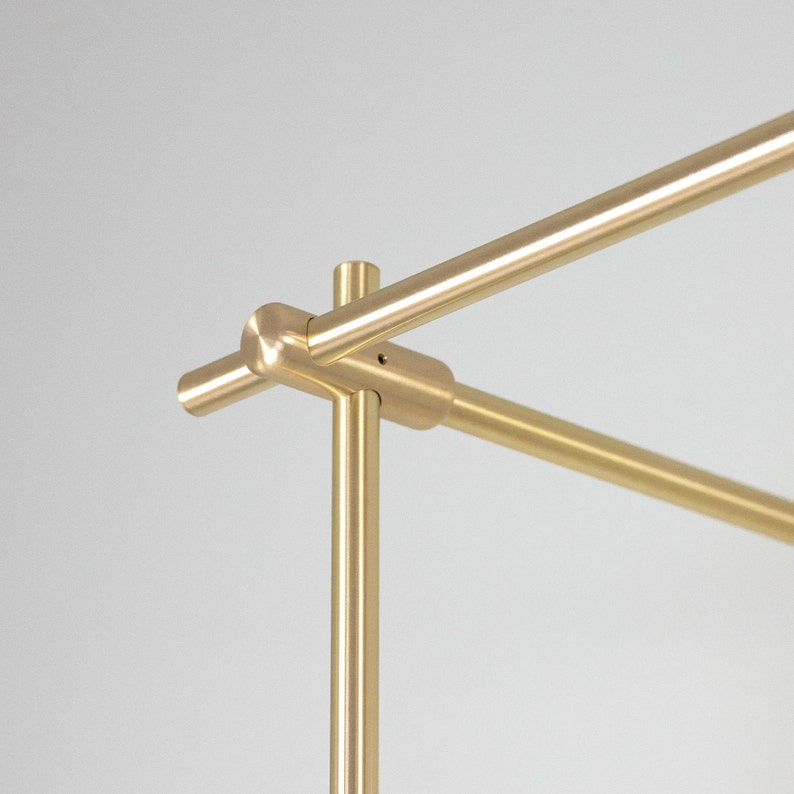 May include: Close-up of a gold metal connector for a clothing rack. The connector is made of two pieces that fit together to create a sturdy and stylish connection.