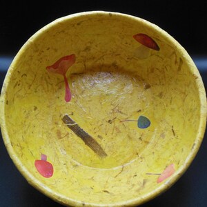 May include: A yellow bowl with a textured surface and a variety of colorful pressed flowers and leaves. The bowl is decorated with red, blue, and yellow flowers.