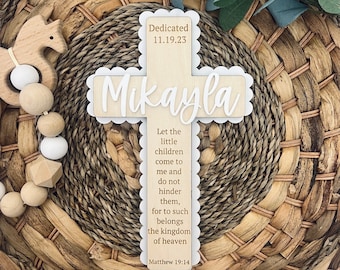 May include: A wooden cross with the name "Mikayla" and the date "11.19.23" engraved on it. The cross also has a scripture verse from Matthew 19:14 that reads "Let the little children come to me and do not hinder them, for to such belongs the kingdom of heaven".