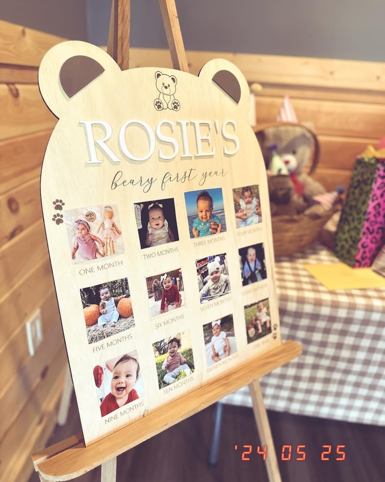 Puede incluir: Un letrero de madera con forma de oso con el texto "ROSIE'S beary first year" y fotos de una ni&ntilde;a a diferentes edades, de un mes a once meses. El letrero est&aacute; en un caballete.