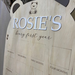 Puede incluir: Un gr&aacute;fico de crecimiento de madera en forma de oso con el nombre "ROSIE'S" y el texto "beary first year". El gr&aacute;fico tiene espacios para fotos o pegatinas para marcar cada mes del primer a&ntilde;o.