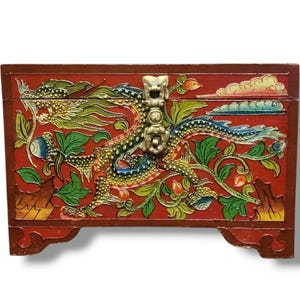 May include: A red wooden box with a detailed dragon design. The box features a brass clasp and is adorned with colourful floral and dragon motifs. The dragon is depicted in green, blue, and gold, with intricate details. The box is rectangular and rests on small feet.