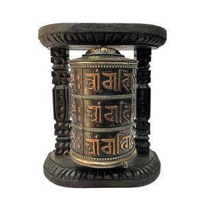 May include: A black wooden prayer wheel with a copper-coloured inscription on a black wooden stand. The inscription reads "Om Mani Padme Hum".
