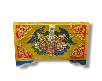 Può includere: Una scatola di legno con un design dipinto in oro, rosso e blu. La scatola ha un coperchio incernierato con un chiavistello in metallo argentato. La parte anteriore della scatola presenta un design floreale stilizzato con una creatura simile a un drago al centro.