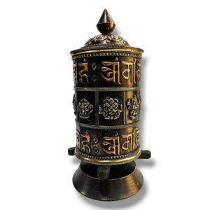 Könnte beinhalten: Ein schwarzes und goldenes Gebetsrad mit filigranen Details und tibetischer Schrift. Das Rad ist auf einem Holzständer mit einer Kupferbasis montiert.