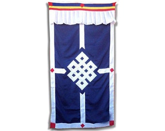 Op de afbeelding: Een blauwe wandhanger van stof met een wit oneindig knoopontwerp en rode en gele bies. De knoop is een symbool van geluk en voorspoed in het Tibetaans boeddhisme.