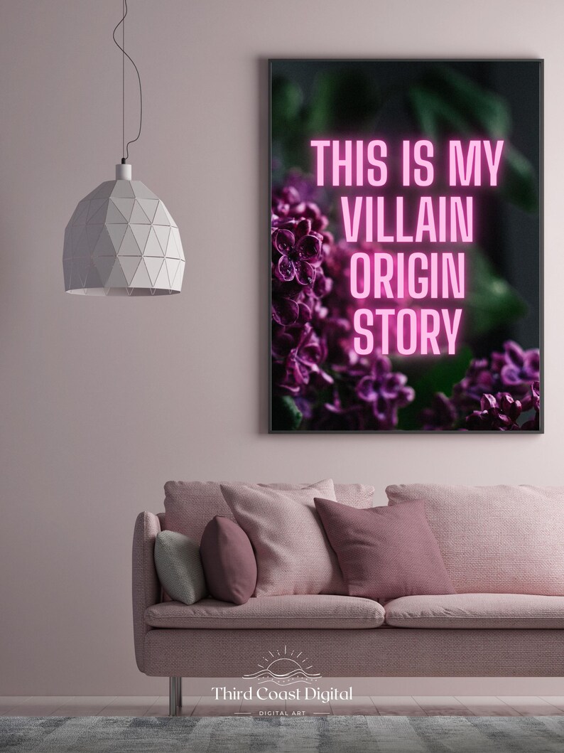 May include: A framed art print with the text "THIS IS MY VILLAIN ORIGIN STORY" in pink neon against a dark background with purple flowers. The print hangs above a pink sofa with pillows.