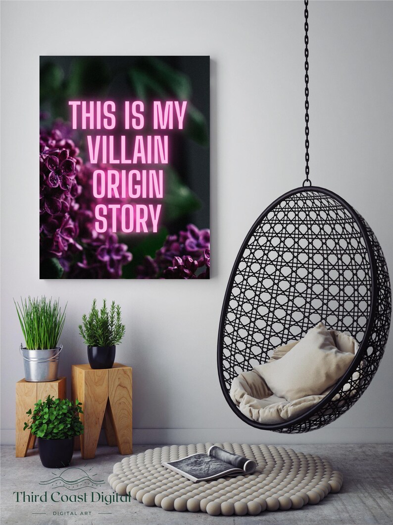 May include: A framed canvas print with the text "THIS IS MY VILLAIN ORIGIN STORY" in pink neon lettering, set against a backdrop of purple flowers. A black hanging chair and small potted plants are also visible.