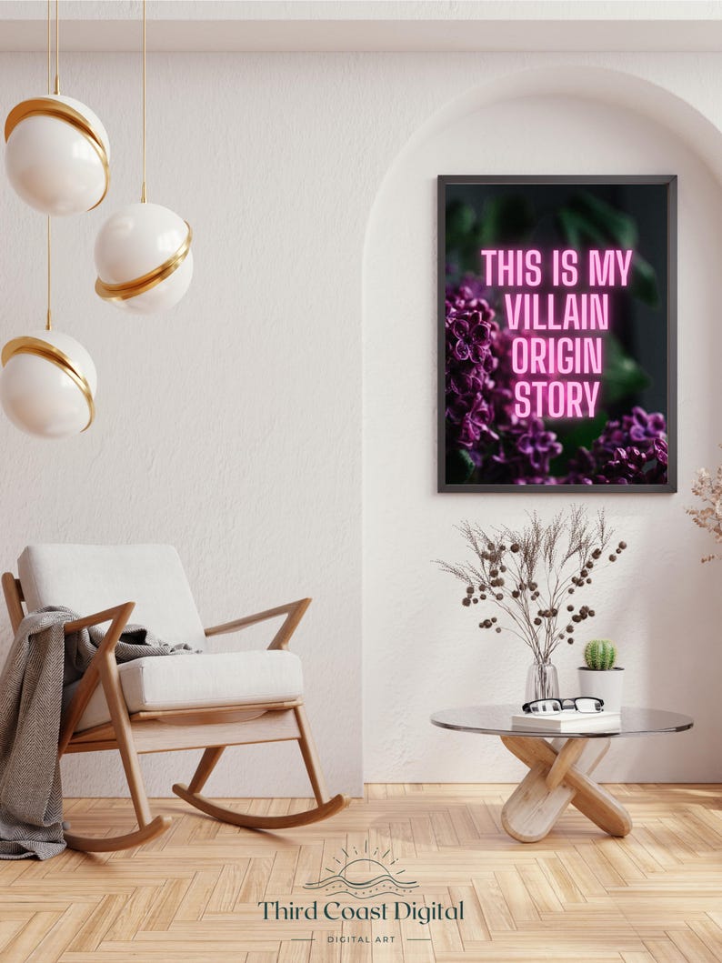 May include: A framed art print with the text "THIS IS MY VILLAIN ORIGIN STORY" in pink neon against a backdrop of purple flowers. The print hangs above a modern living room scene with a rocking chair, coffee table, and decorative lighting.