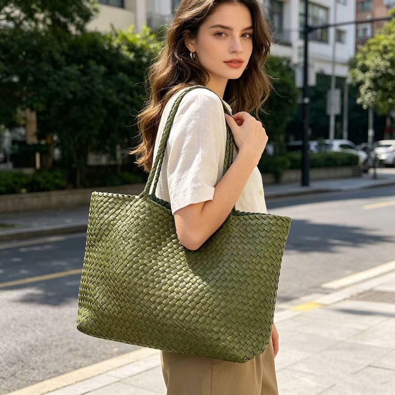 May include: A woven olive green tote bag with matching handles. The bag has a rectangular shape and a textured surface. The tote is carried over the shoulder. The bag is made of a durable material and is suitable for everyday use.