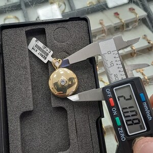 K&ouml;nnte beinhalten: Ein goldener Anh&auml;nger mit einem runden, flachen Design und einem einzigen klaren Stein in der Mitte. Der Anh&auml;nger wird mit einer digitalen Schieblehre gemessen, die 20,00 mm anzeigt.