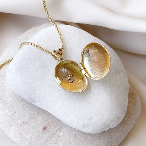 K&ouml;nnte beinhalten: Eine goldene Halskette mit einem Anh&auml;nger in Form eines Medaillons, mit einem herzf&ouml;rmigen Verschluss. Das Medaillon ist ge&ouml;ffnet und zeigt ein kleines, rundes, goldfarbenes Inneres.