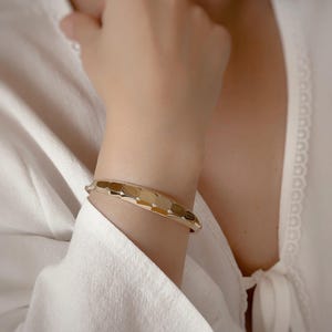 Könnte beinhalten: Ein goldfarbenes Armband mit geometrischem Design. Das Armband besteht aus miteinander verbundenen, rechteckigen Formen.